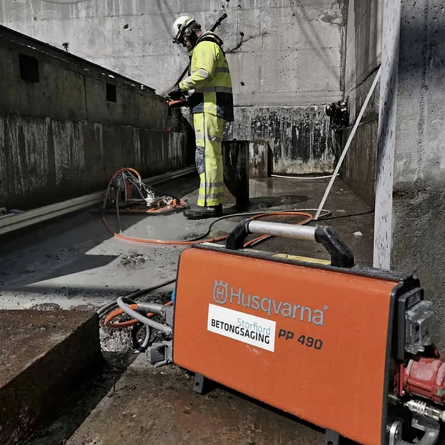 Arbeider i refleksklær med betongsag og Husqvarna-utstyr på byggeplass